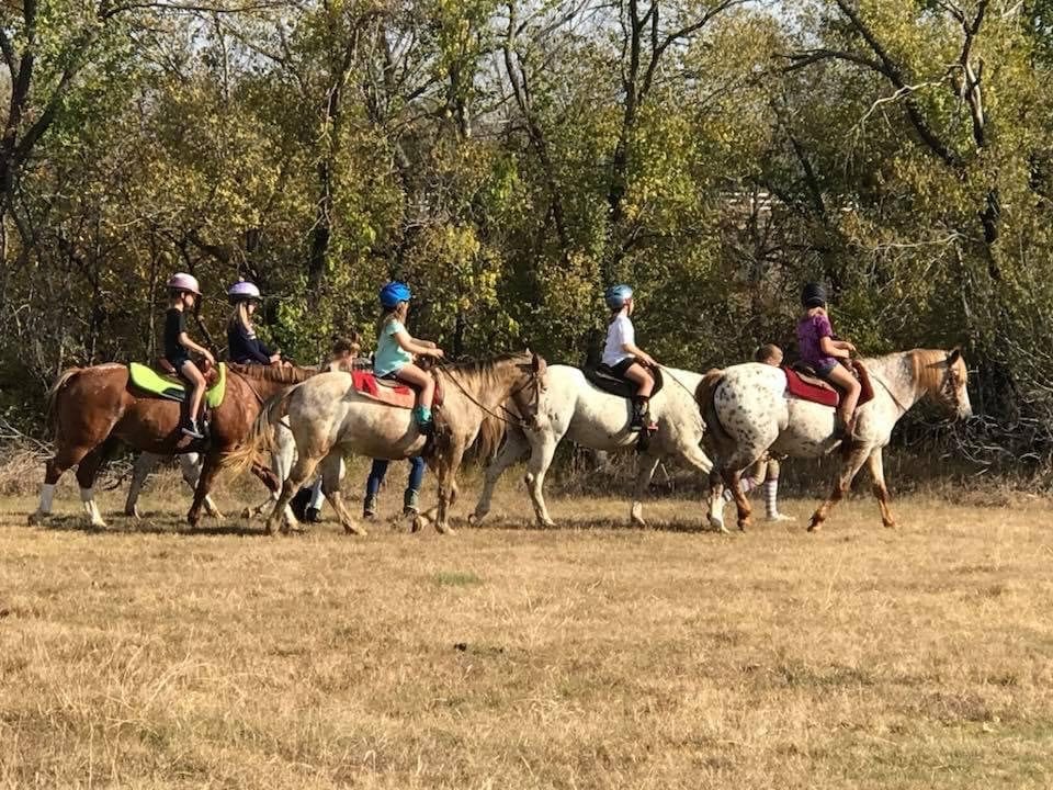 A line of riders on a trail ride in the field.